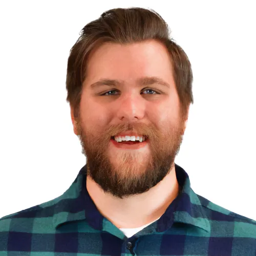 Front-end engineer, Dave Berning in a teal plaid flannel shirt and grey pants with his hands in his pockets, smiling and looking at the camera.